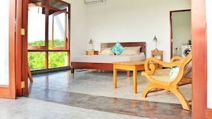 Quarto com cama, mesas de cabeceira, uma cadeira de madeira e vista através de uma janela grande.