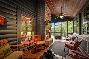 A log cabin with a stone fireplace, wooden furniture, and a balcony with a view of greenery.
