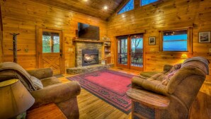 A log cabin interior with a fireplace, wooden walls, and a cozy seating area. - Adventure Us- Aska Area, Lake Views, Dog Friendly (Blue Ridge)