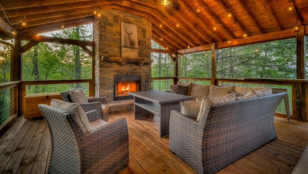 A cozy wooden deck with wicker furniture, a fireplace, and large windows overlooking a forest. - Adventure Us- Aska Area, Lake Views, Dog Friendly (Blue Ridge)