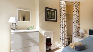 A hotel room with a bed, a dresser, a mirror, a fireplace, and a window with curtains. - Highfield Grove -  a serviced house that sleeps 4 guests  in 2 bedrooms (Nottingham)