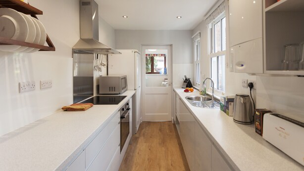 A modern kitchen with white cabinets, a stainless steel range hood, a microwave, and a sink. - Highfield Grove -  a serviced house that sleeps 4 guests  in 2 bedrooms (Nottingham)