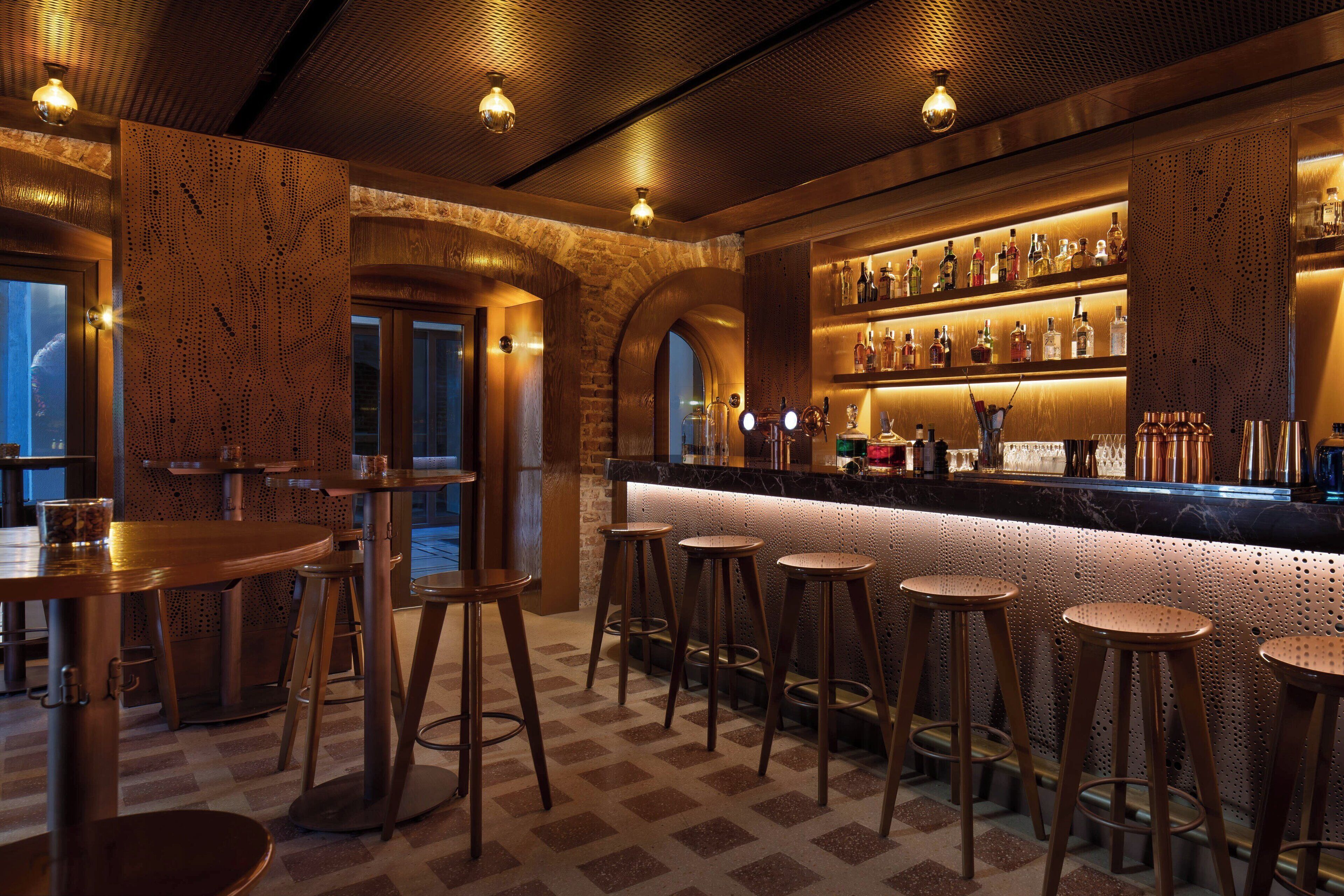 Zona de bar con taburetes de madera, barra y estanterías llenas de botellas.
