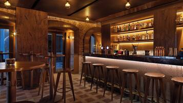 Zona de bar con taburetes de madera, barra y estanterías llenas de botellas.