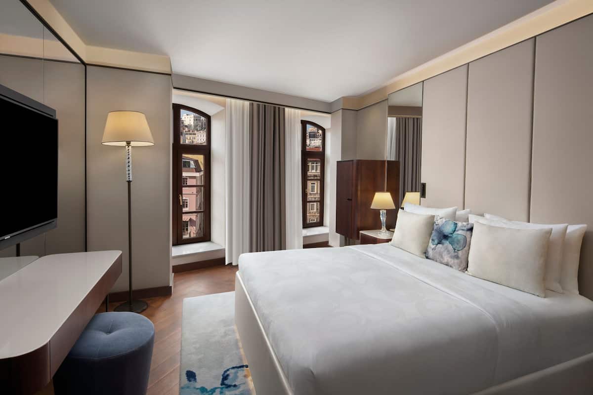 Una habitación de hotel con cama, escritorio, televisor y ventana con cortinas.