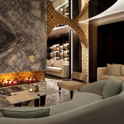 A modern lounge area with a marble fireplace, leather sofas, and a brick accent wall.