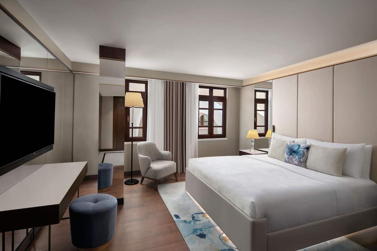 Habitación de hotel con una cama grande, televisor de pantalla plana, escritorio, silla y lámpara.