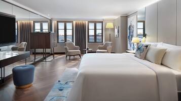 A modern hotel room with a large bed, two armchairs, a desk, and a TV.