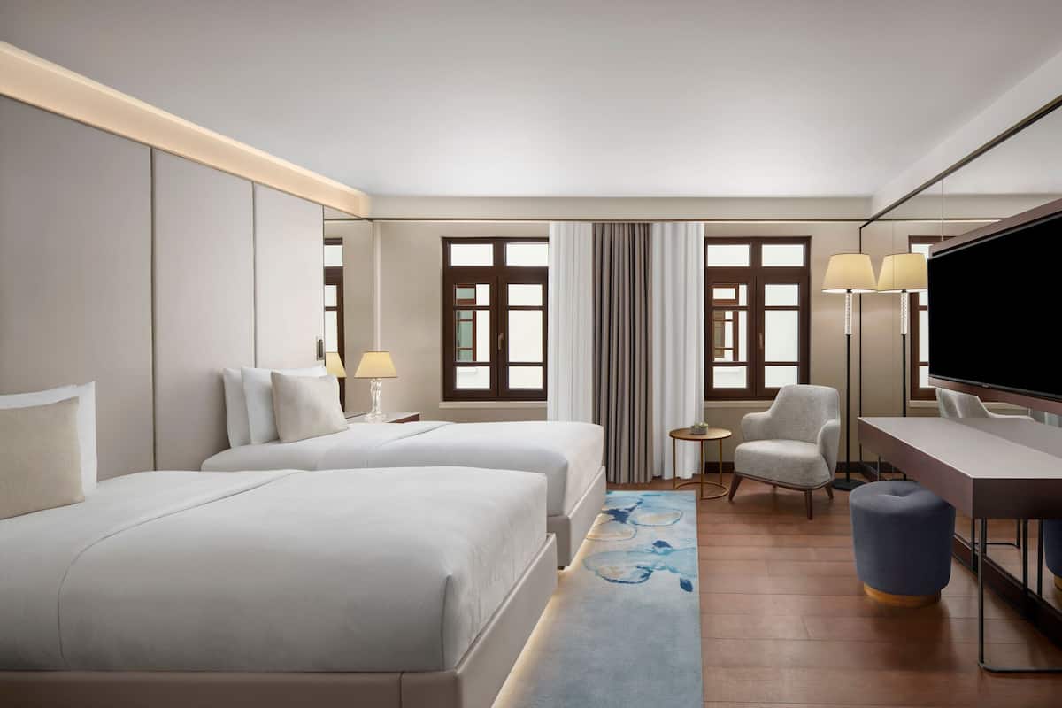 Habitación de hotel con dos camas, un escritorio, una silla, un televisor y una ventana con cortinas.