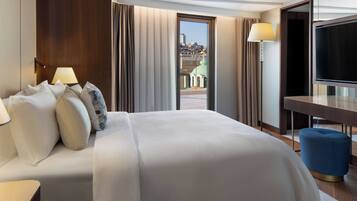 Ein Hotelzimmer mit einem großen Bett, einem Schreibtisch, einem Fernseher und Blick auf eine Stadtlandschaft durch ein Fenster.