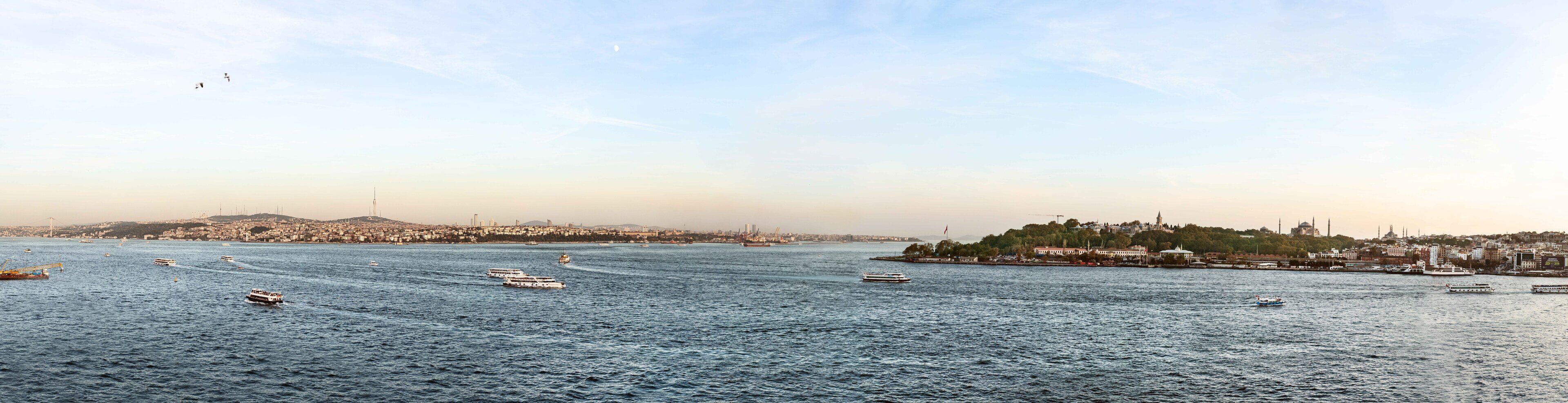 A view of a cityscape with a large body of water, boats, and a distant hill with buildings.