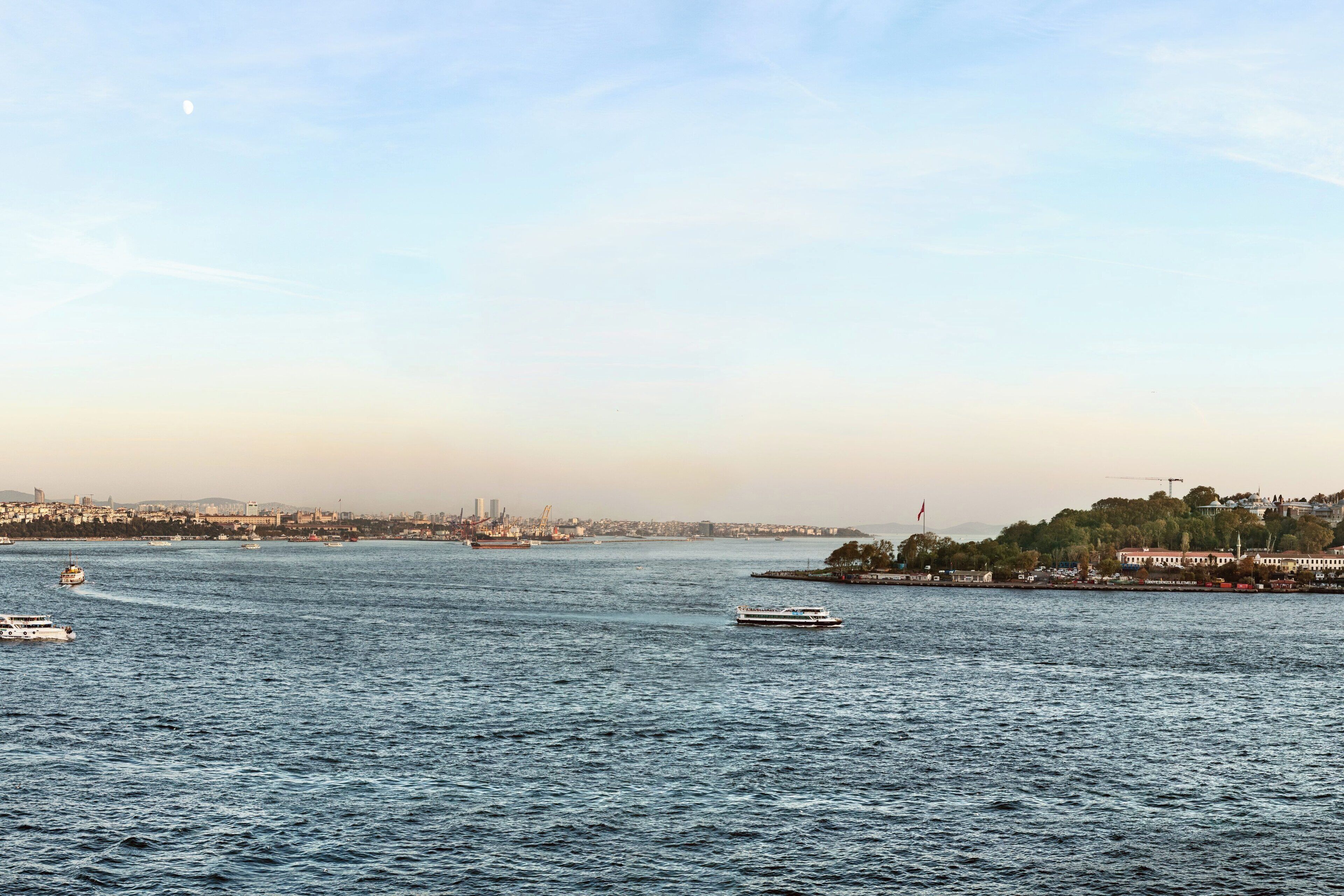 A river with boats, a city skyline, and a hill with buildings.