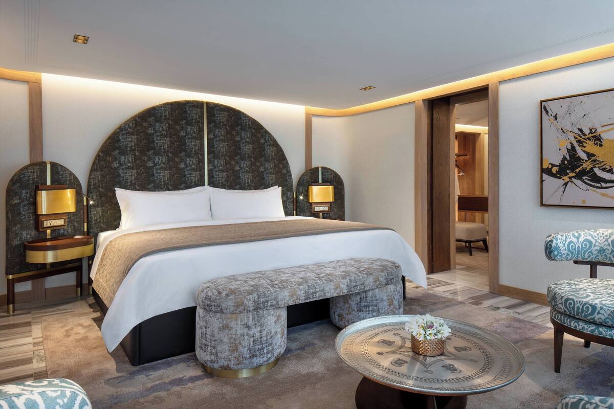 Una habitación de hotel moderna con una cama grande, una mesa de centro redonda, un banco y una silla.