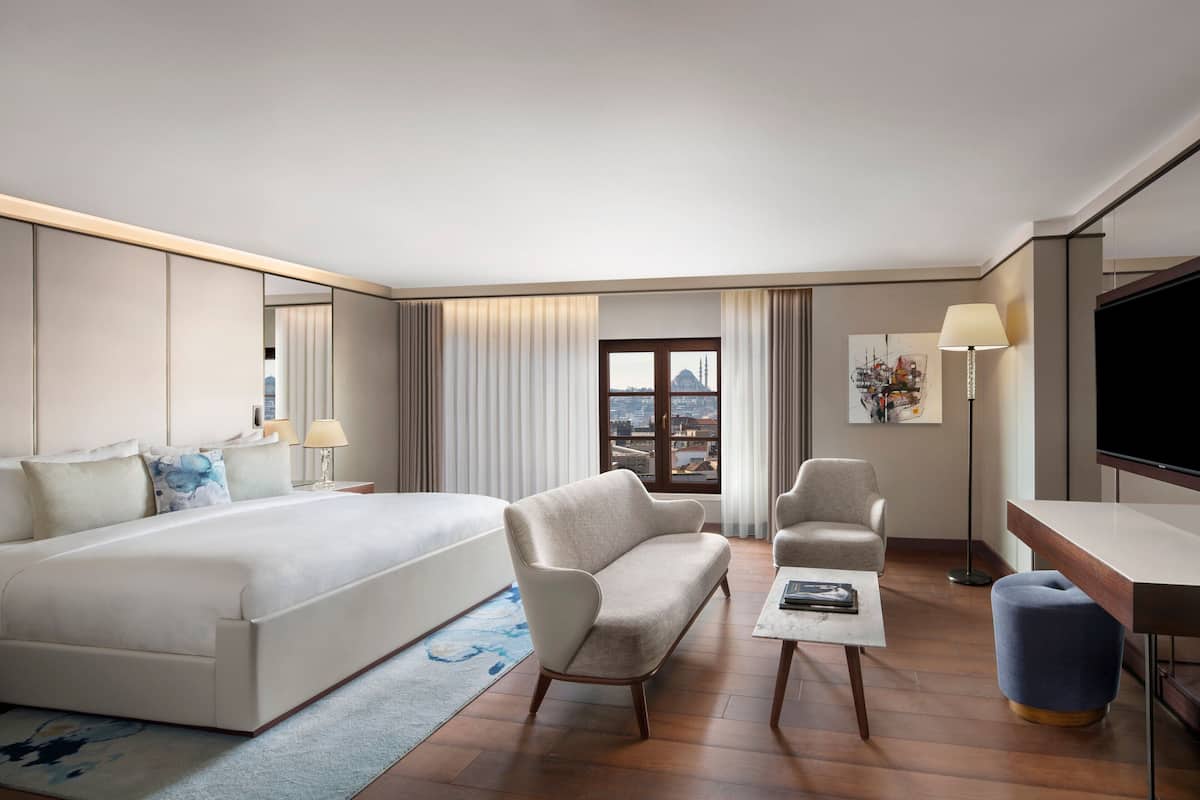 Una habitación de hotel moderna con una cama grande, dos sillones, un escritorio y un televisor.