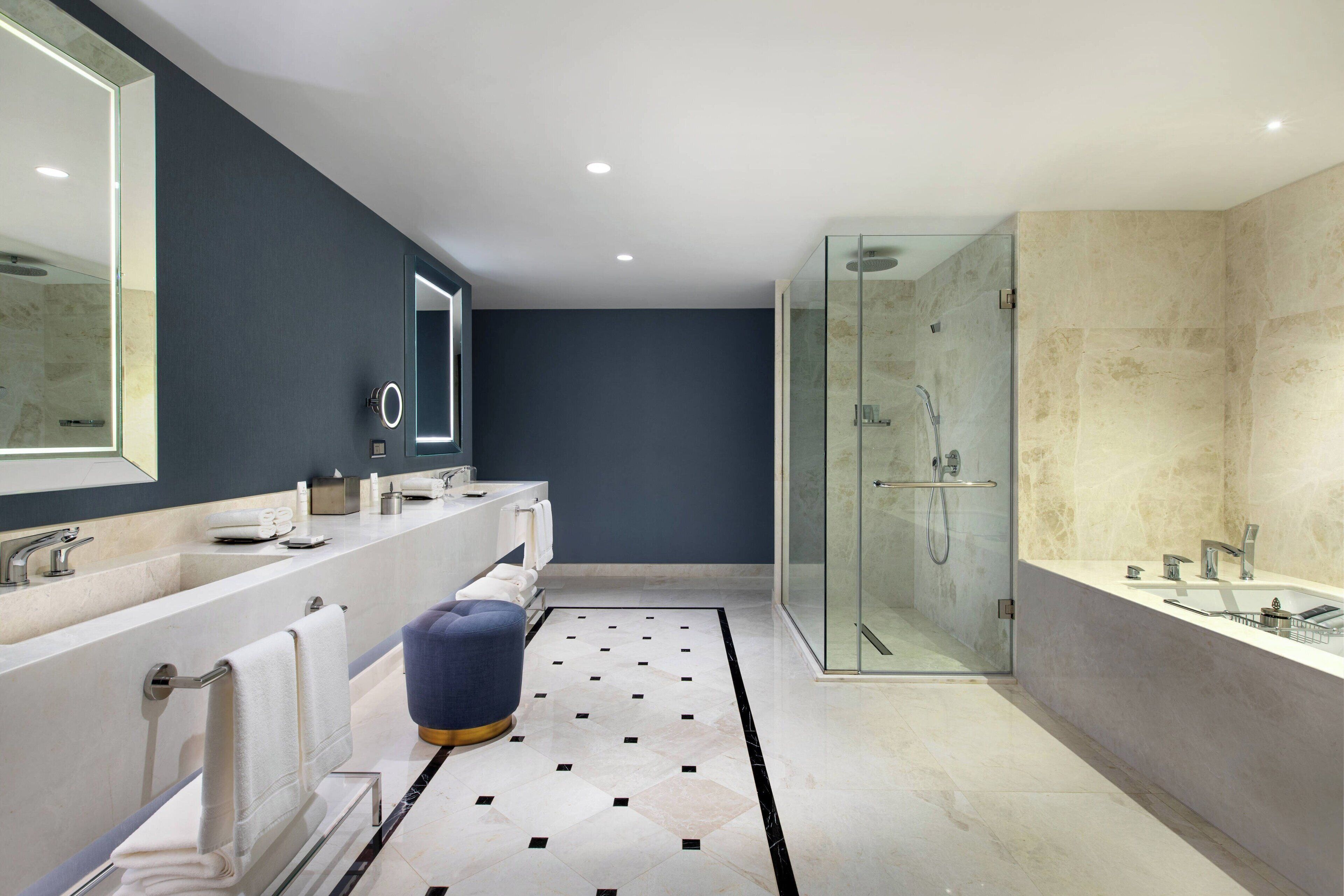 A modern bathroom with a glass-enclosed shower, a large mirror, and a marble floor.