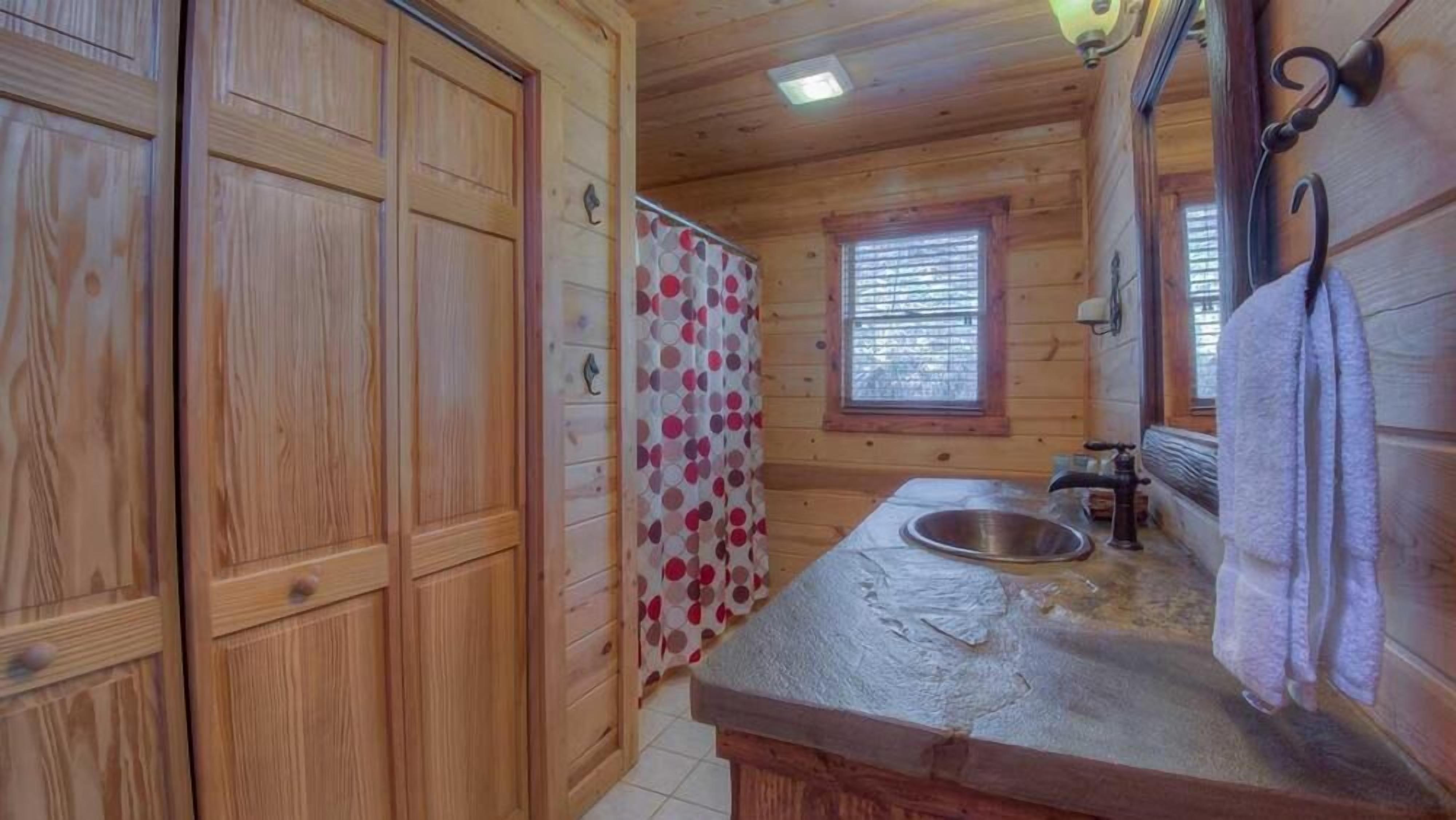 A wooden cabin bathroom with a sink, a window, and a shower curtain.