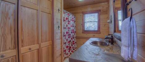 A wooden cabin bathroom with a sink, a window, and a shower curtain.