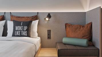 Ein modernes Hotelzimmer mit einem Bett, einem Nachttisch, einer Wandlampe und einer kleinen Sitzecke mit Kissen.
