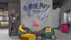 Een moderne lounge met groene banken, een geel poefje, een roze koffer en een muur met tekst in graffiti-stijl.