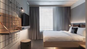 Une chambre d’hôtel moderne équipée d’un lit, d’un téléviseur fixé au mur, d’un petit tabouret et d’une fenêtre avec des rideaux.