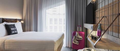 A hotel room with a bed, a suitcase, a camera, and a wall-mounted shelf.