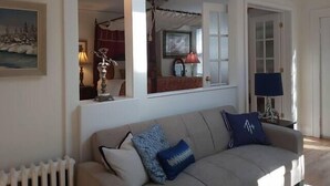 A living room with a beige sofa, a painting, and a window with a view of another room. - 1930'S Charming & Enchanted Unit By Waterfalls (Armdale)