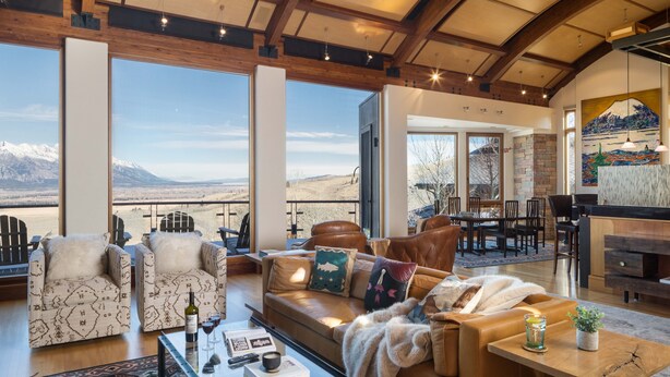 Un salon spacieux doté de grandes fenêtres, d’une cheminée et d’un coin repas offrant une vue sur les montagnes.