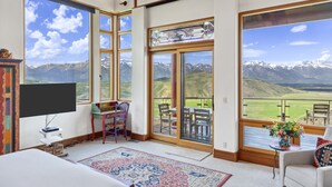 Une pièce spacieuse dotée de grandes fenêtres offrant une vue sur les montagnes, d’un téléviseur à écran plat, d’un coin repas et d’un espace salon confortable.