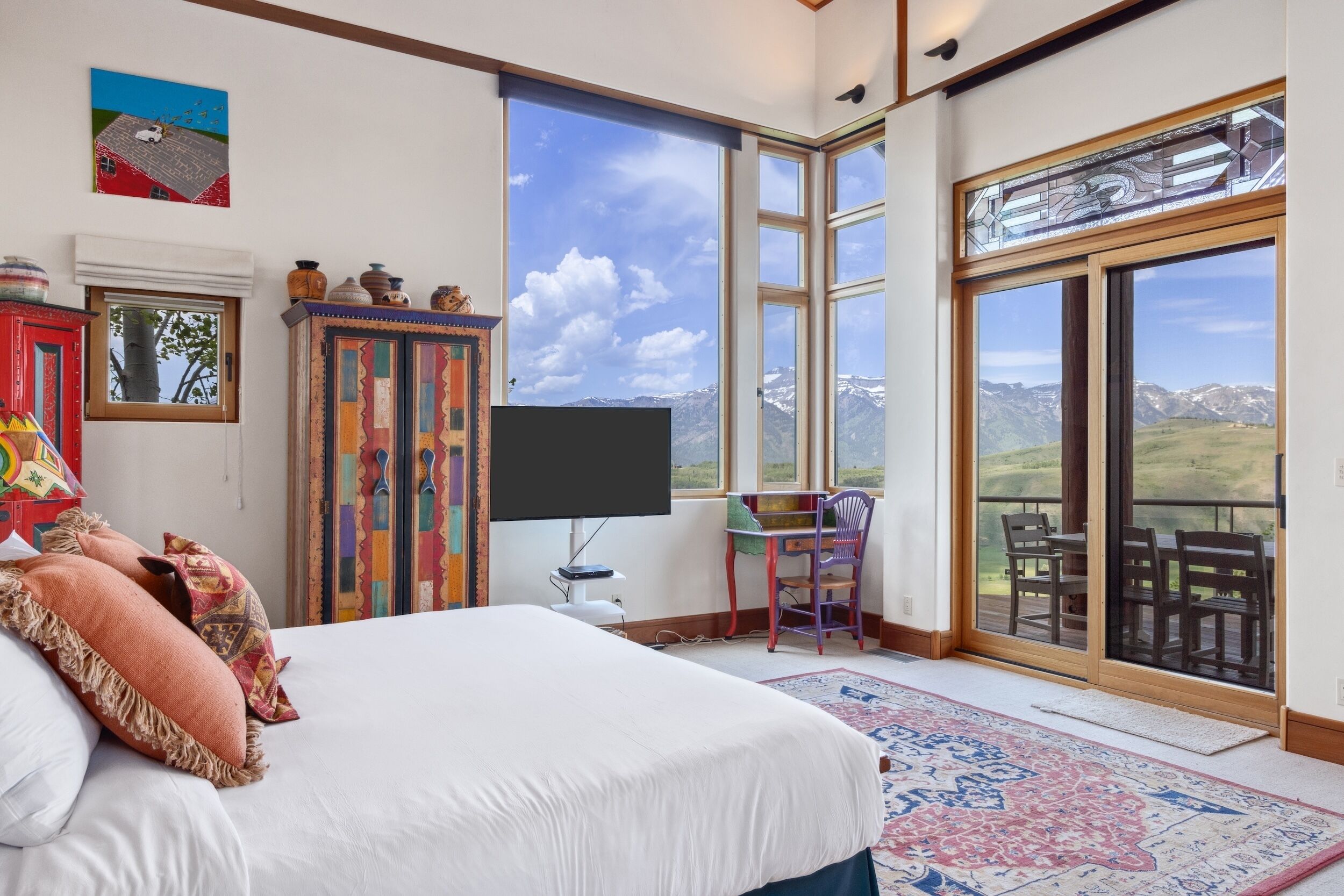 A bedroom with a large bed, a TV, a window with a mountain view, and a sliding glass door to an outdoor deck.