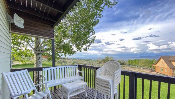 Una terraza de madera con mobiliario exterior blanco, vista a una casa y un árbol.