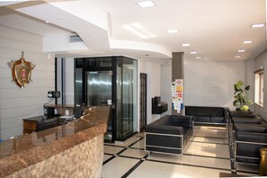A modern reception area with a marble counter, a coat of arms on the wall, and a seating area with black sofas.