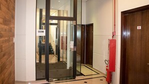 Entrada de un hotel con puerta de vidrio, extintor y una puerta de madera a la derecha.