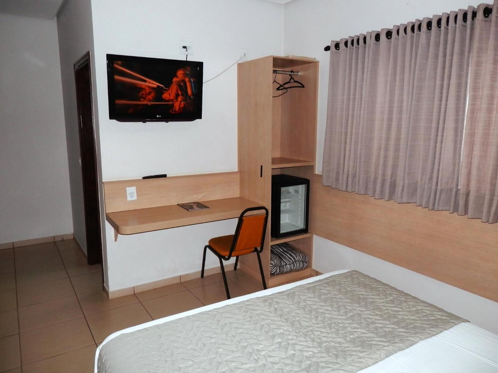A bedroom with a bed, a desk, a chair, a TV, and a wardrobe.