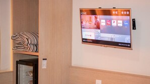 Habitación de hotel con un televisor de pared mostrando la pantalla de inicio, un minibar y una mesita con una bandeja y algunos objetos.