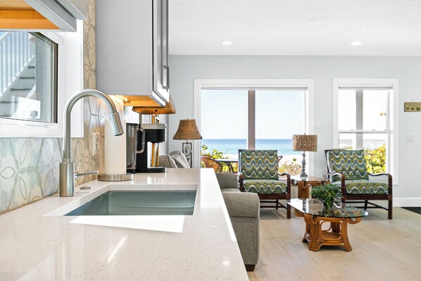 Una cocina moderna con una isla grande, vista al océano y un área de estar con sillas y una mesa.