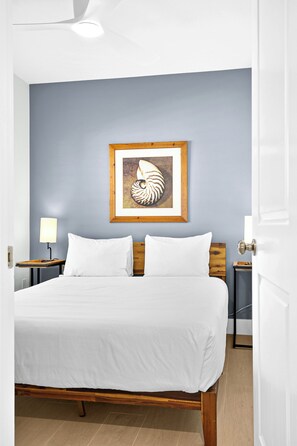A neatly made bed with white linens, a framed artwork on the wall, and a wooden headboard.