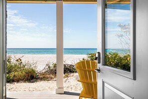 Vista a la playa a través de una puerta, con una silla amarilla en el exterior.