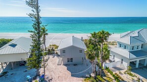 A beachfront property with a central house, two smaller buildings, and a sandy beach.