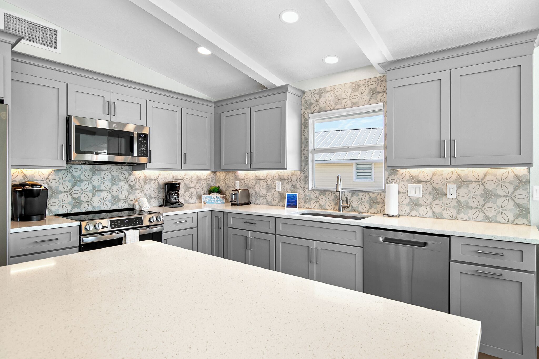 A modern kitchen with grey cabinets, a stainless steel microwave, a gas stove, and a dishwasher.