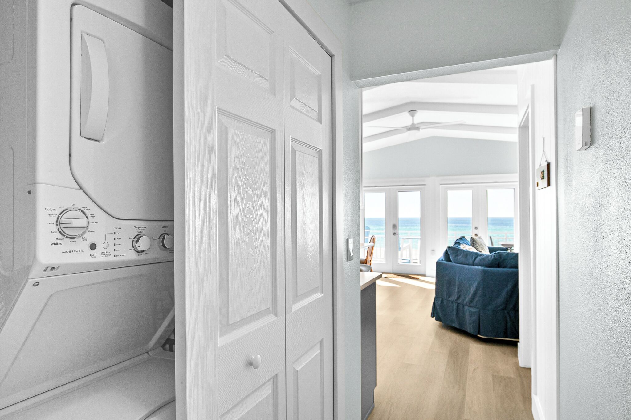 A laundry room with a washing machine, a hallway leading to a living area with a view of the ocean.