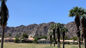 Un parcours de golf offrant une vue dégagée sur les montagnes en arrière-plan, entouré de palmiers et d’immeubles résidentiels.
