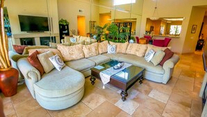 Un salon spacieux avec un grand canapé d’angle, une table basse en verre et un téléviseur à écran plat.