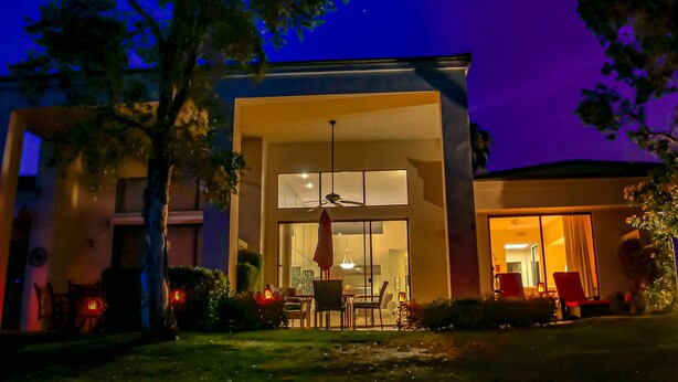 Une maison moderne dotée d’une grande baie vitrée, d’un coin repas avec des chaises et une table, et d’un ventilateur de plafond bien visible.