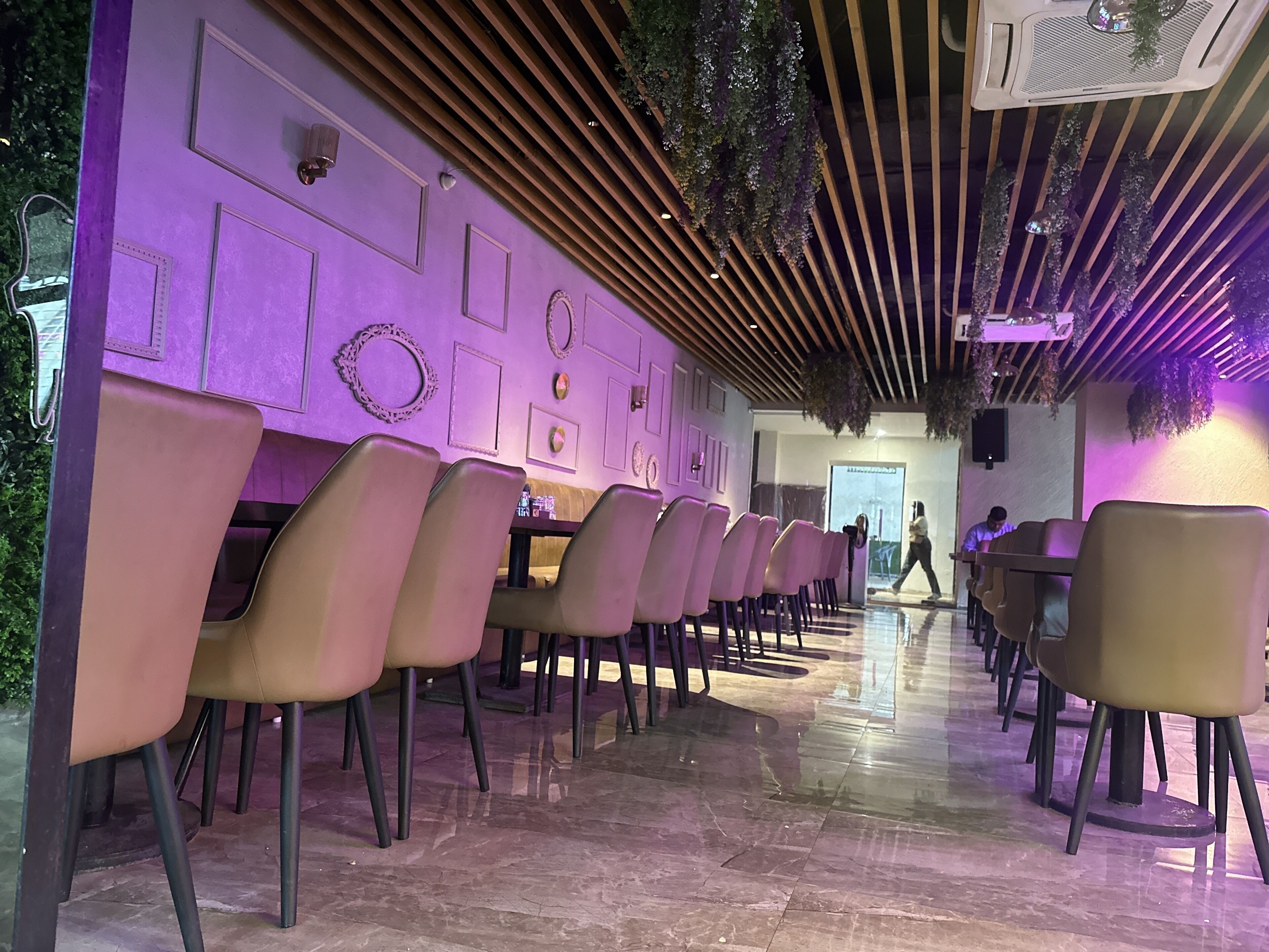 A modern interior with a row of chairs and tables, a wooden slatted ceiling, and decorative wall elements.