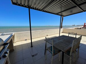 Un espace extérieur abrité, aménagé avec des sièges, et offrant une vue sur la plage et l’océan.