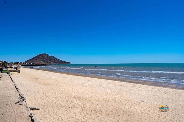 Une plage avec une montagne en arrière-plan, un ciel dégagé et une rive sablonneuse.