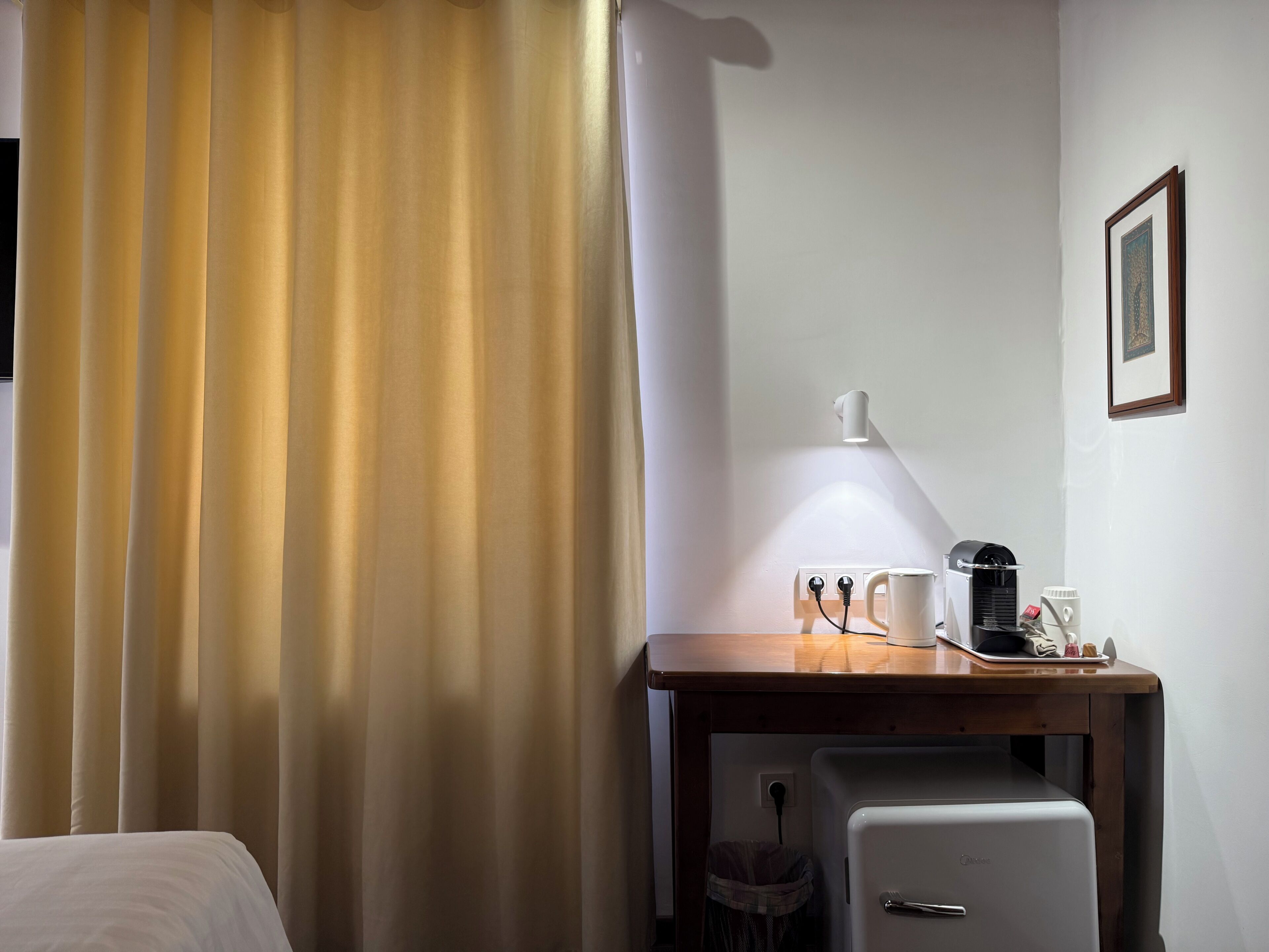 Et hotelværelse med en seng, et skrivebord med kaffemaskine, en lampe og et lille køleskab.