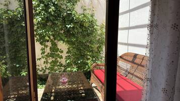 A wicker table with a glass top and a red cushion, a wicker chair, and a wall covered with green ivy.