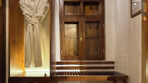 A wooden bench with a slatted design, a wooden cabinet with glass doors, and a towel hanging on a rack. - Usman Heritage Hotel (Bukhara)