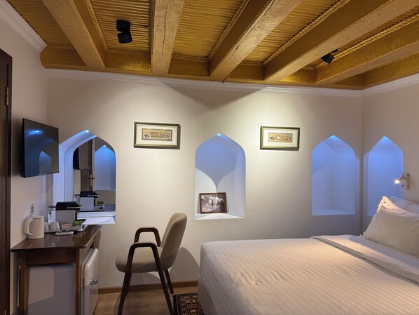 Un dormitorio con una cama, un escritorio con una silla, un televisor y cuadros en la pared.